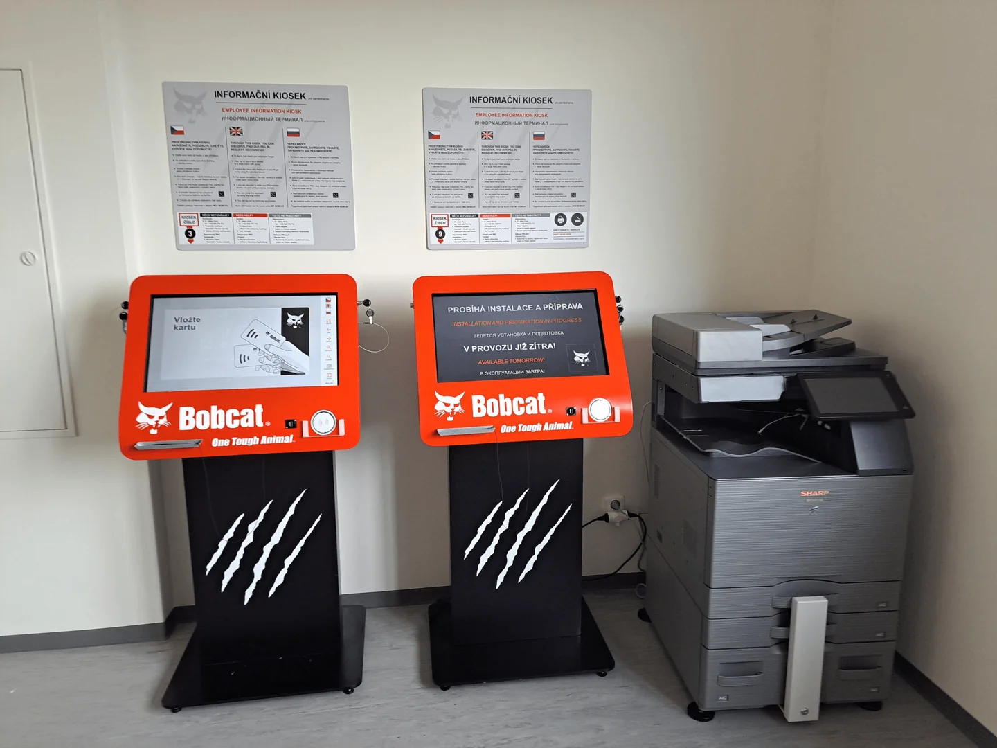 Dvojice kiosků Doosan Bobcat vedle multifunkční tiskárny